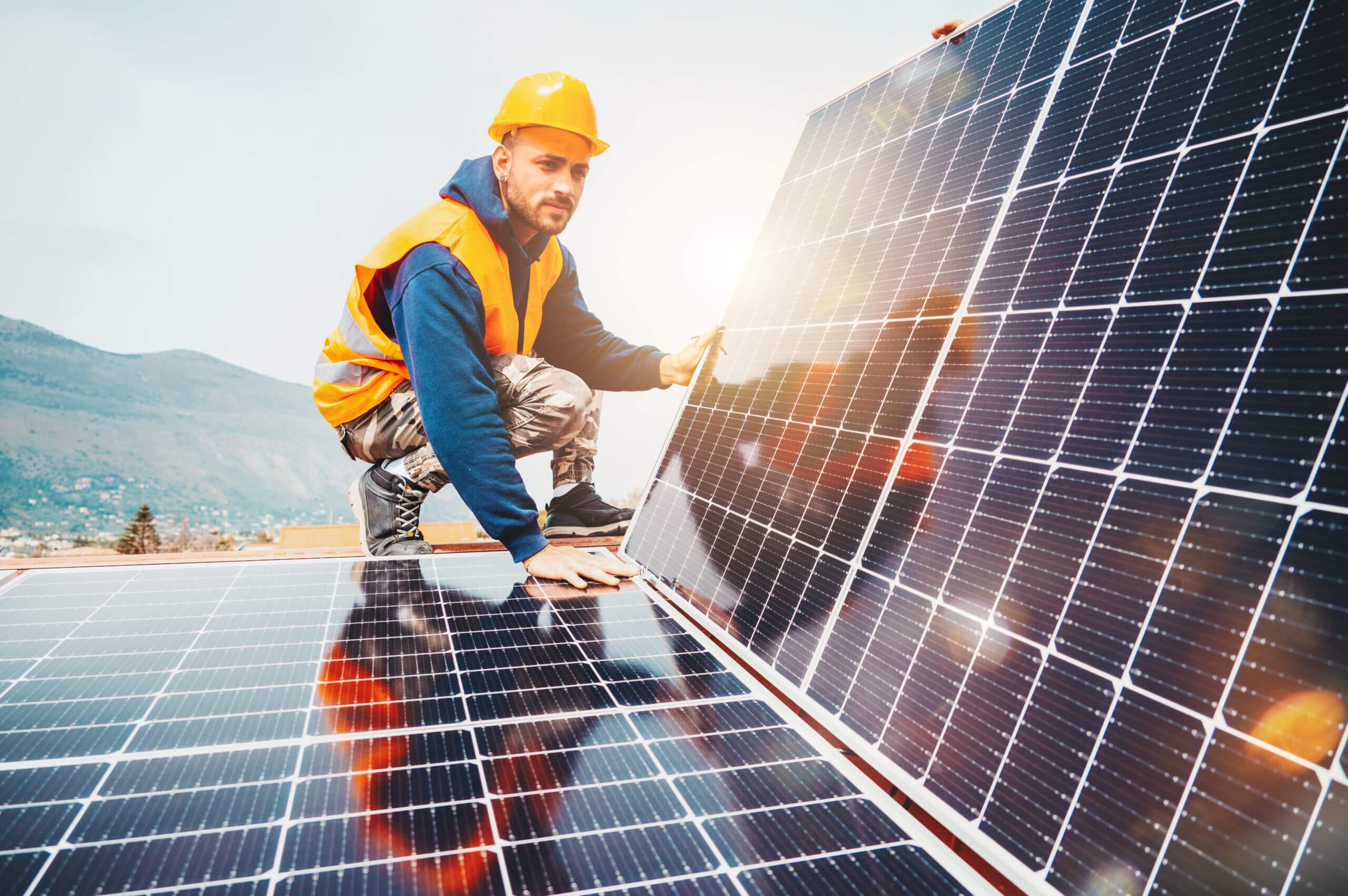 Man with hard hat and orange vest assembles solar panel in the mountains