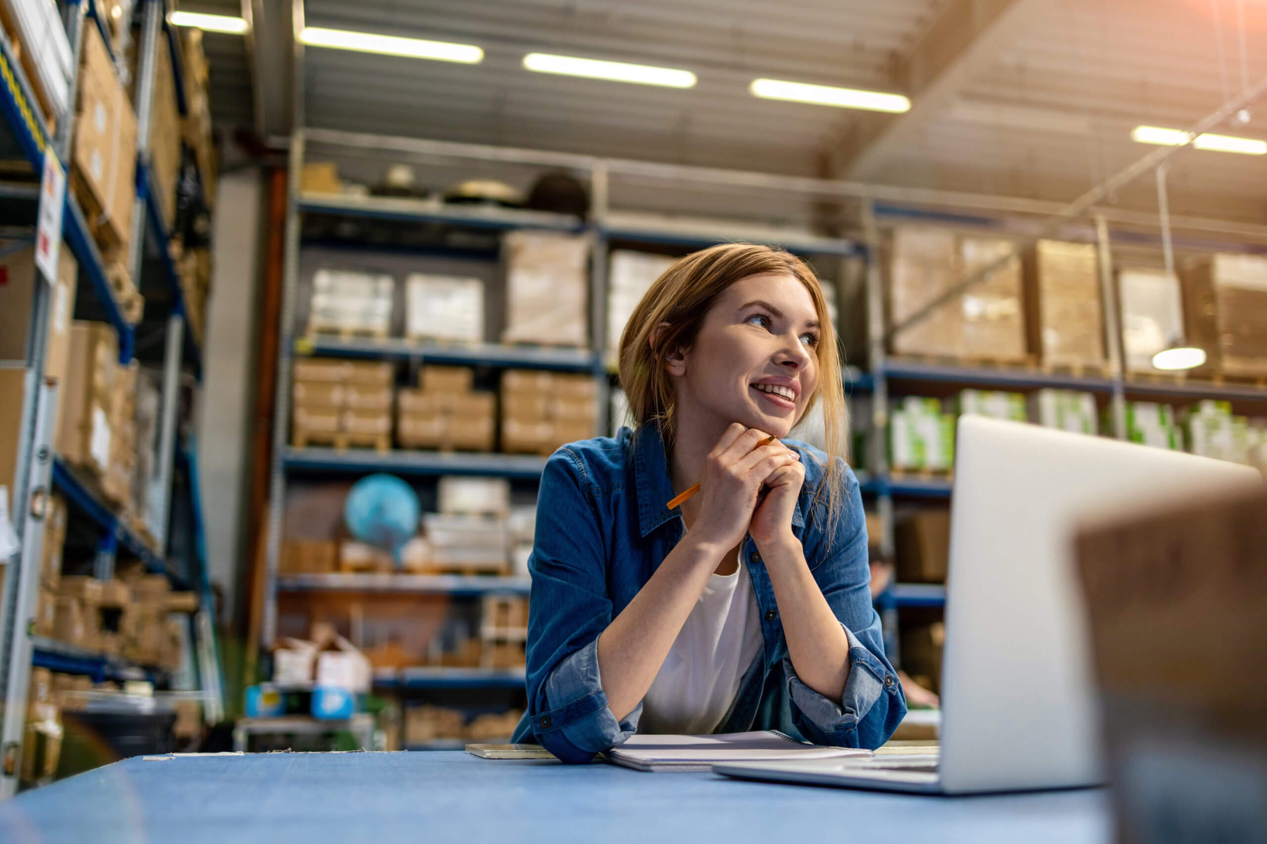 woman working in warehouse with a laptop looking up and smiling